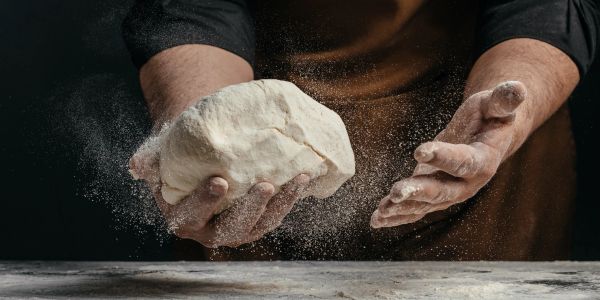 Hands dusted with flour hold a ball of dough.