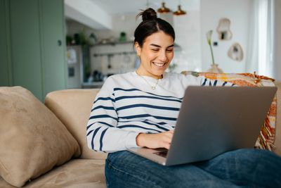 Smiling woman using laptop on couch.