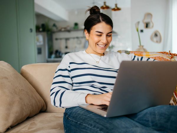 Woman smiling while using laptop on couch.