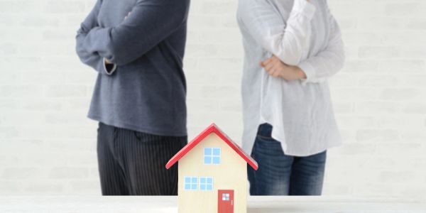 Couple standing back-to-back with a model house in front.