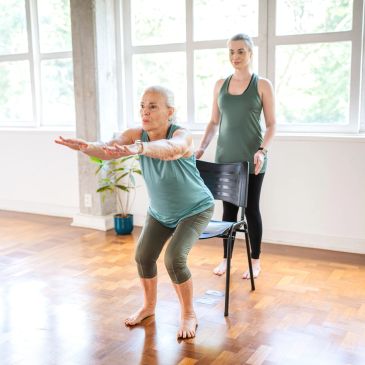 Older woman doing squats with trainer support.
