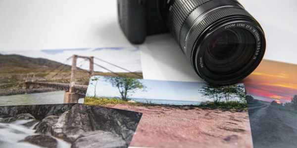 Camera lens with printed landscape photos on a table.