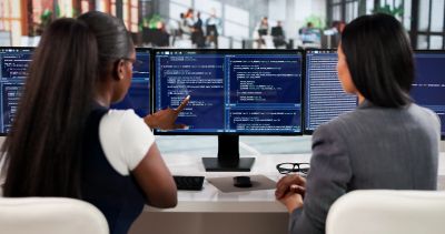 Two women coding on a computer at work.