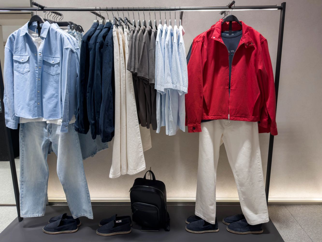 Clothing rack displays casual shirts, pants, and shoes in coordinated colors with a standout red jacket.