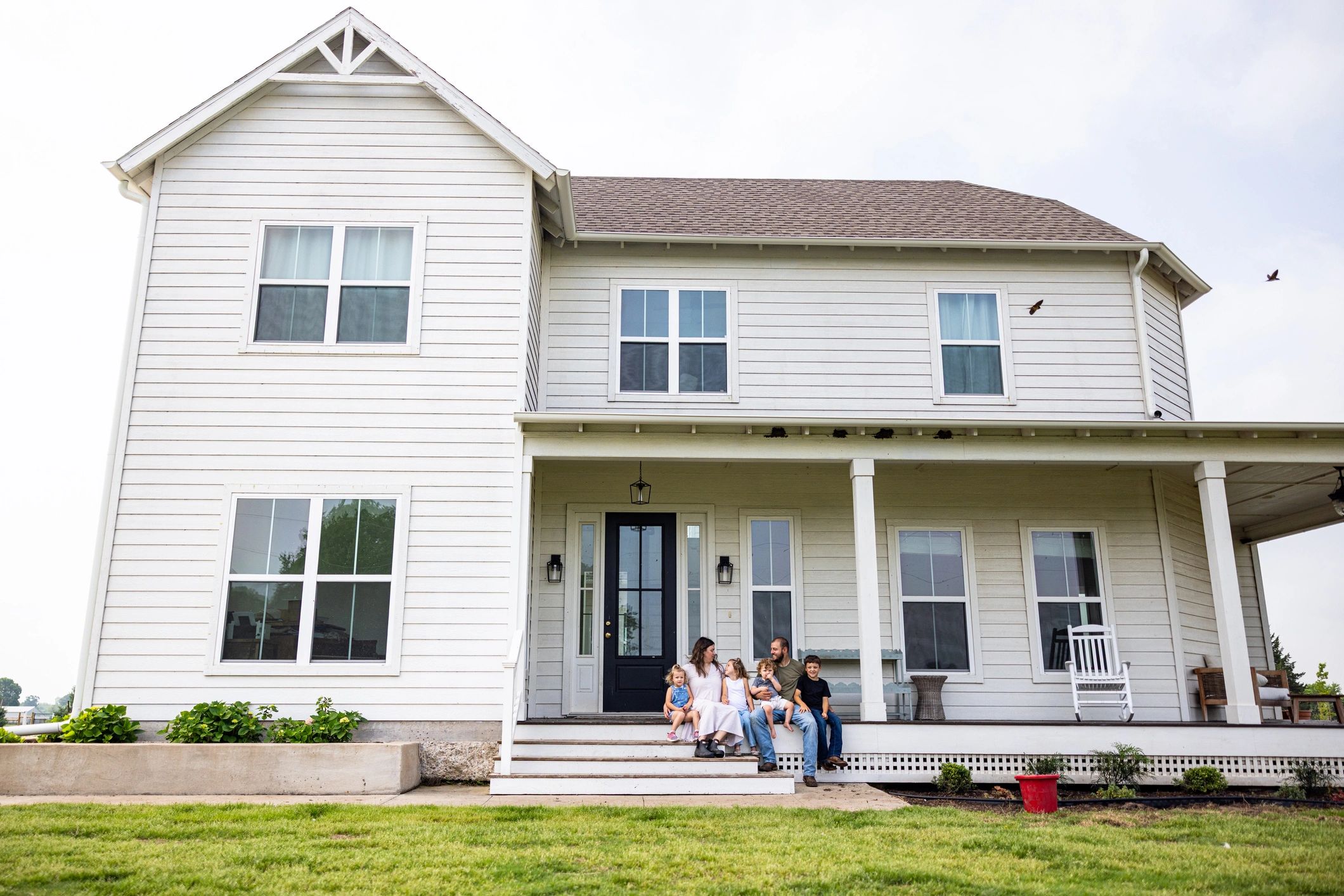 Family sitting on the porch of a large white house.
