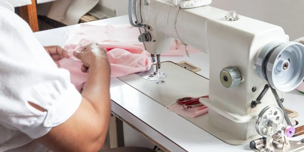 Person sewing pink fabric using a sewing machine.