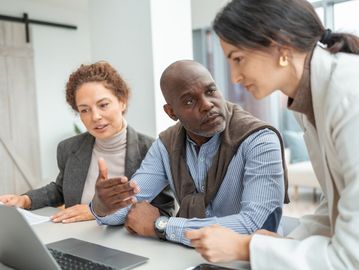 Three professionals engaged in a discussion around a laptop.