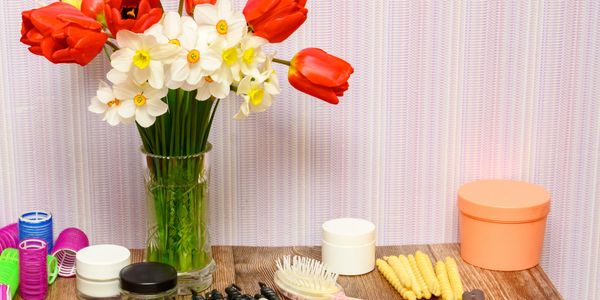 A vase with red tulips and white daffodils on a wooden table with beauty products.