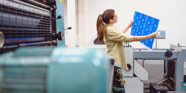 Woman inspecting a printed sheet in a printing press facility.