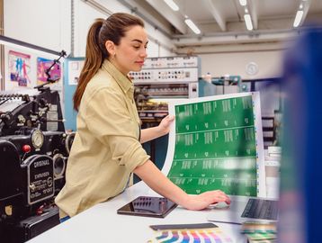 A woman inspects printed sheets in a printing workshop.