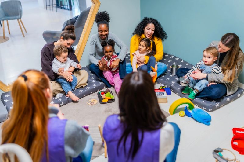 Diverse parents and young children sitting on mats with a teacher in a modern, inclusive daycare, interacting, playing, and learning together in a warm, nurturing classroom setting