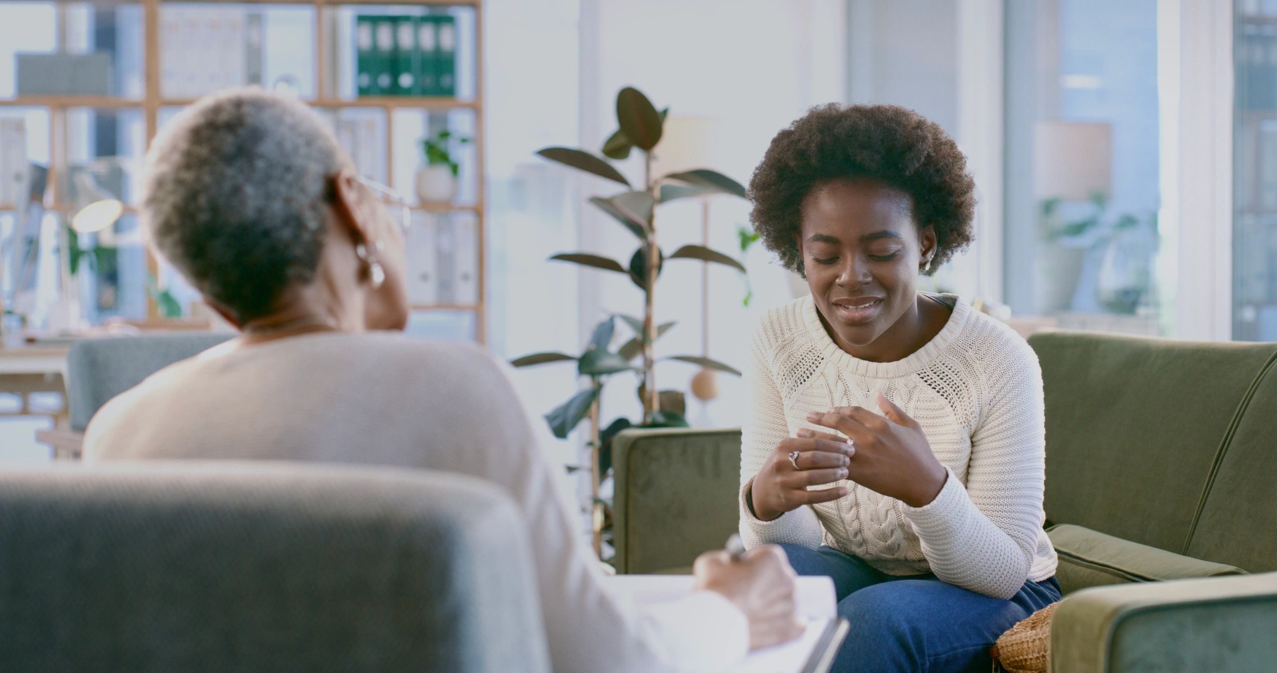 Smiling client in a cream knit sweater talking with a therapist beside a large plant