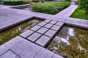 Modern stone pathway over a shallow water feature in a garden.