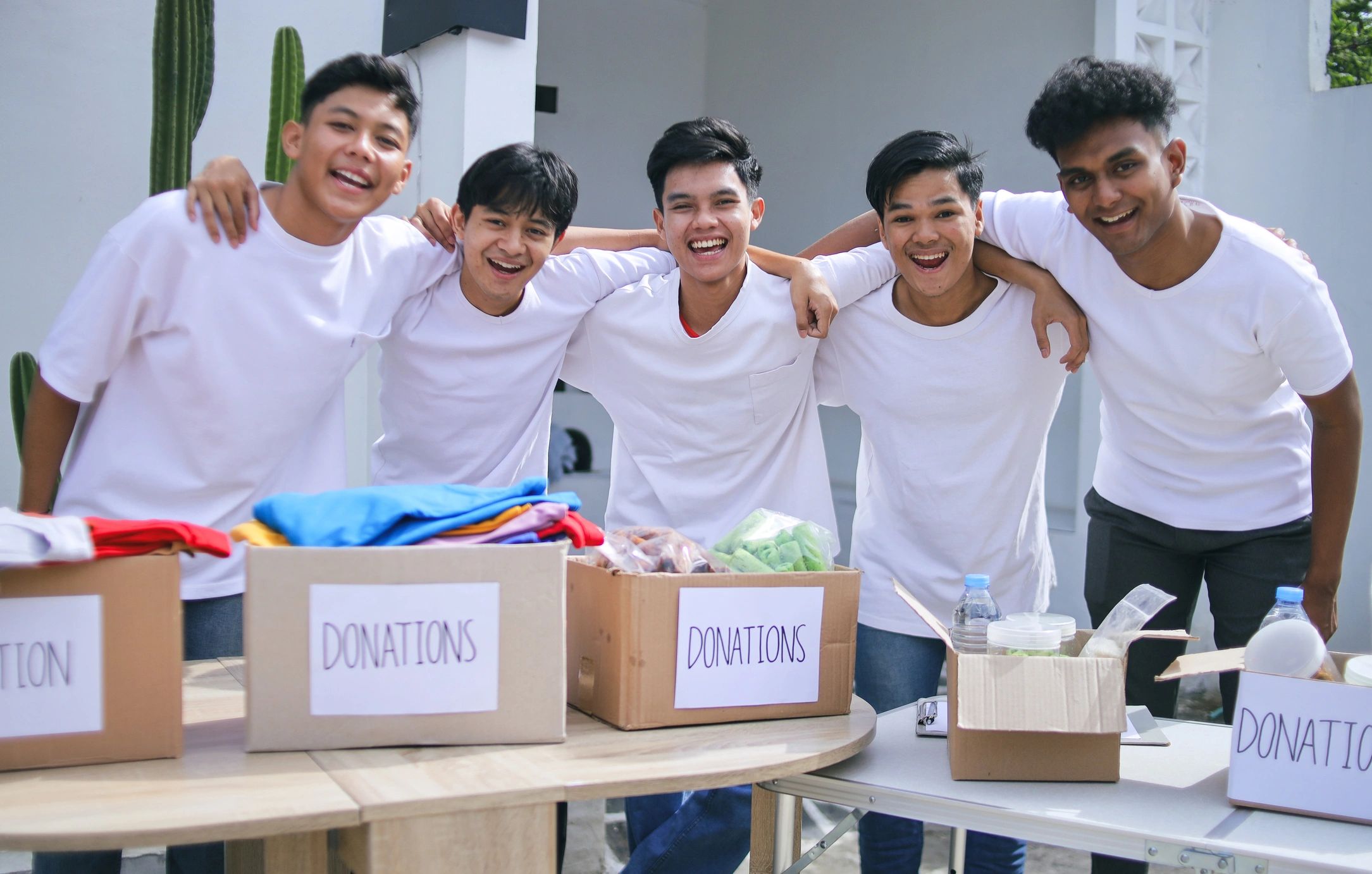 Five friends smiling behind donation boxes.