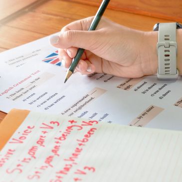A person writing on a grammar test paper with notes beside it.