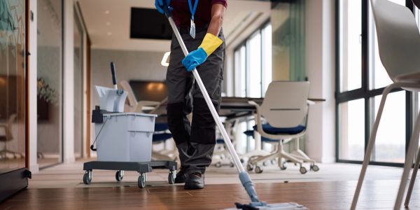 Person mopping office floor with cleaning equipment nearby.