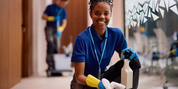 Smiling cleaning professional in blue uniform holding spray bottle and cloth.