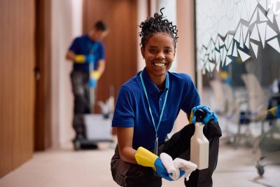 Smiling cleaner holding cleaning supplies indoors.