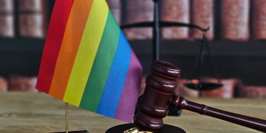 LGBTQ+ flag with a judge's gavel and scales of justice.