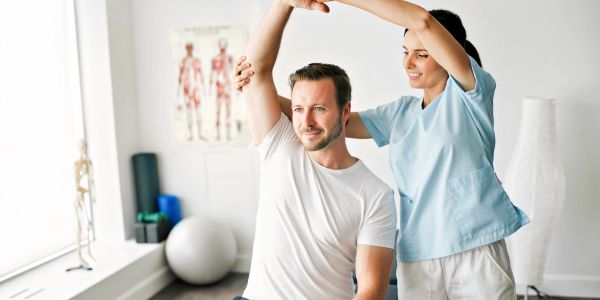 Physical therapist assists man with arm stretch.