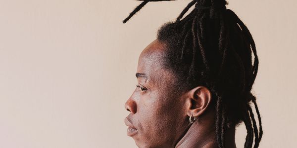 Side profile of a person with dreadlocks against a plain background.