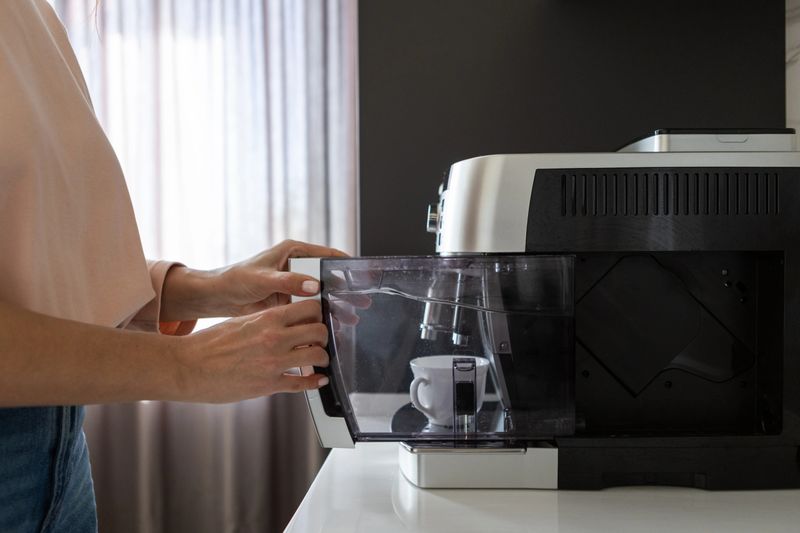 Close up of adult person placing water reservoir into coffee machine. Everyday kitchen routine, appliance use and beverage preparation concept.