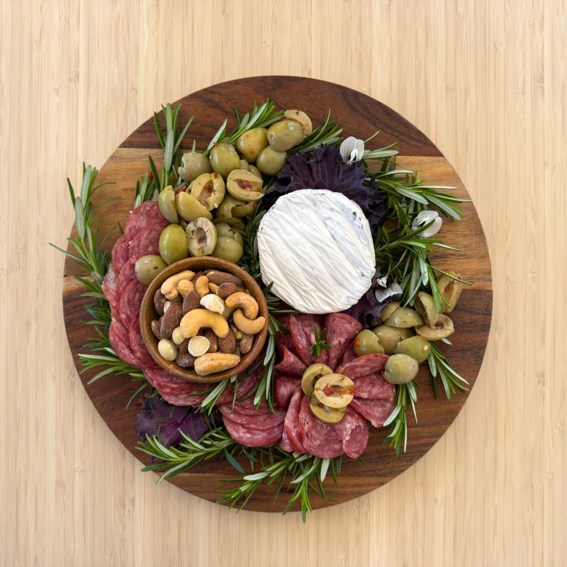 Overhead view of a timber gourmet charcuterie board or cheese platter with various meats, olives, nuts and cheese