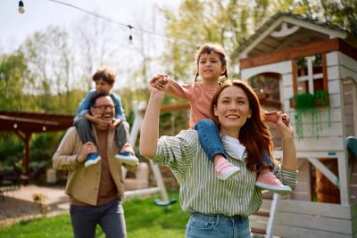 Happy family enjoying outdoors with children playing on parents' shoulders.