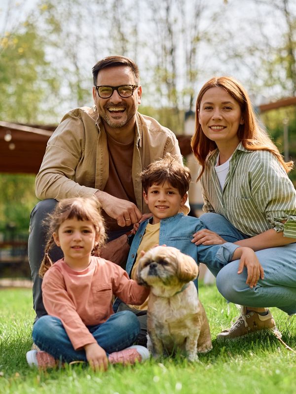 Happy family of four with their small dog outdoors on a sunny day.