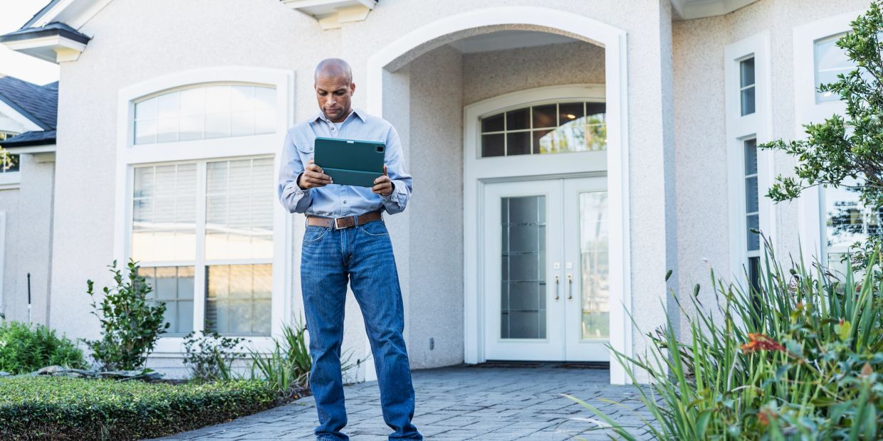 Man standing outside a house using a tablet.