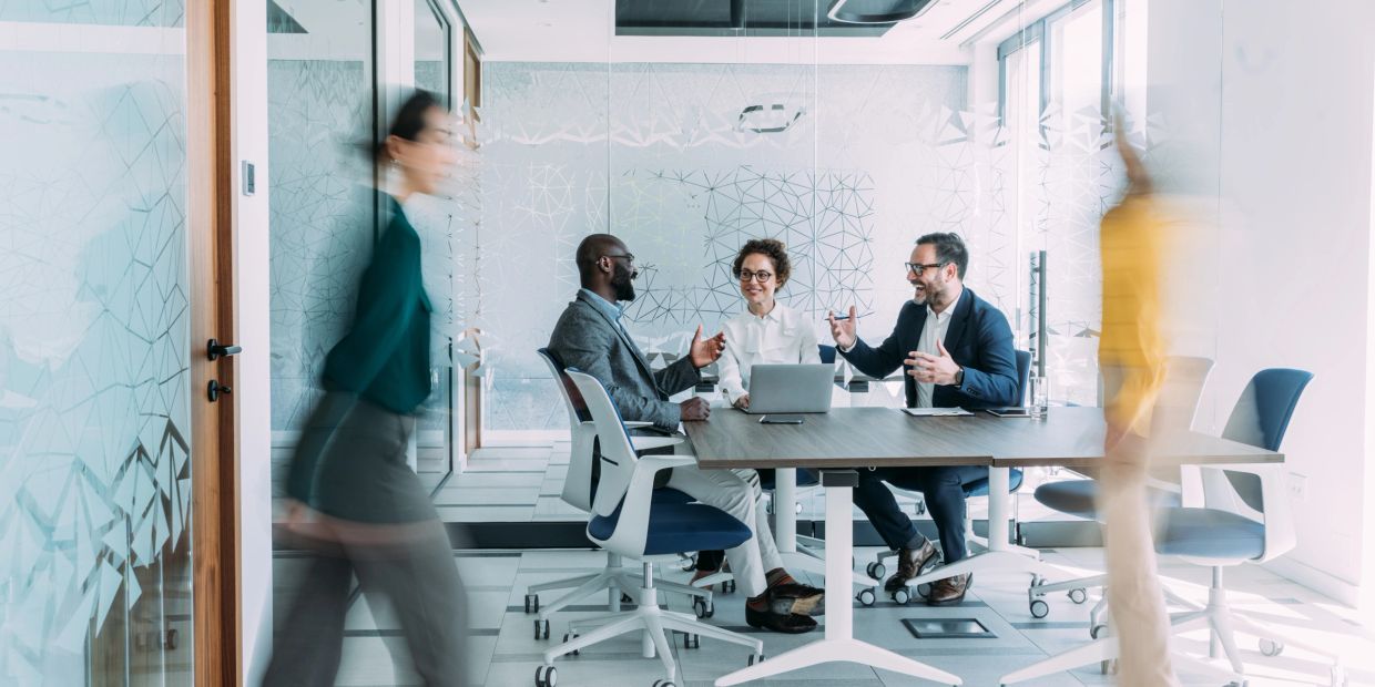 Three professionals discussing in a glass office.