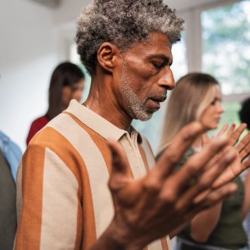 Man praying with raised hands in a group.