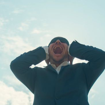 Man in suit shouting with hands on ears.