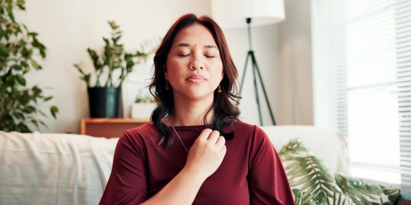 A woman meditates peacefully with eyes closed and hand on chest.