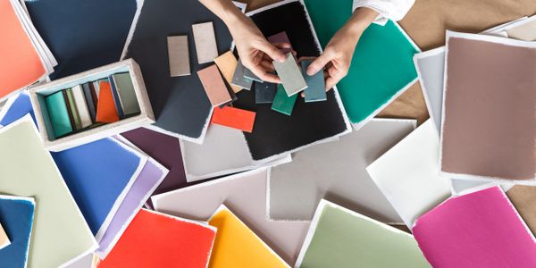 Hands selecting color swatches among many vibrant paper samples.