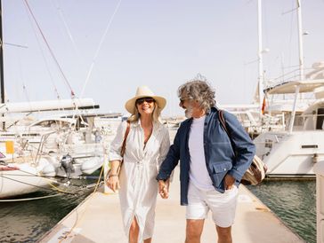 An older couple walking along a dock holding hands. Happy and smiling together.