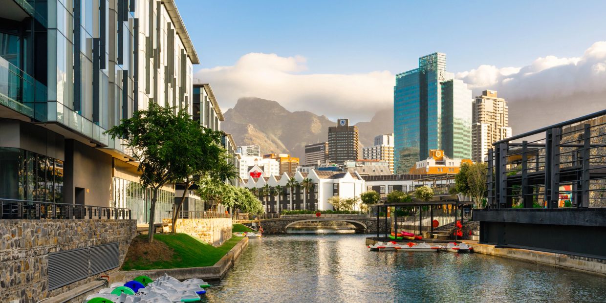 Urban canal with modern buildings and mountains in the background.
