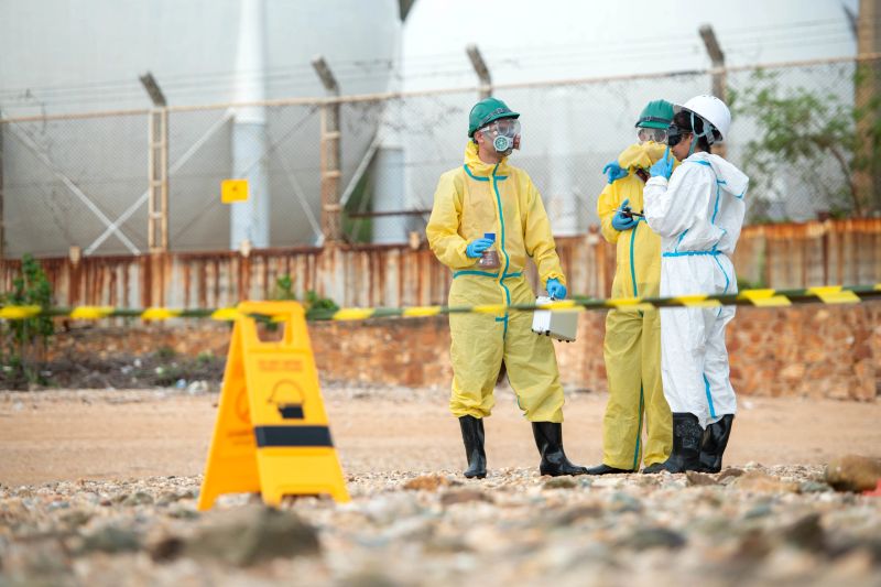 Group of hazmat engineers collecting contaminated water samples from industrial wastewater discharge near drainage canal