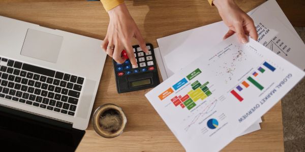 Person using calculator and analyzing charts with laptop and coffee.