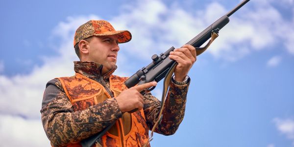 Hunter aiming a rifle under a blue sky.