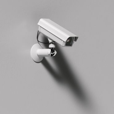 White security camera mounted on a gray wall casting a shadow.