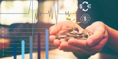 Hands holding coins with a small plant and financial charts in the background.