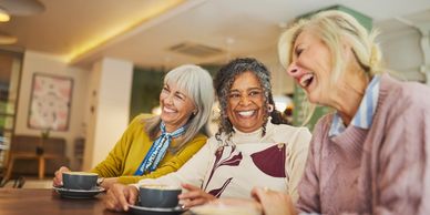Three elderly women laughing together over coffee.
