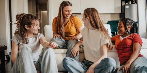 Four young women sitting and chatting happily in a cozy living room.
