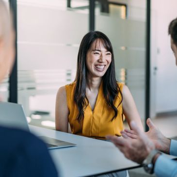 Smiling woman in a yellow blouse during a meeting.