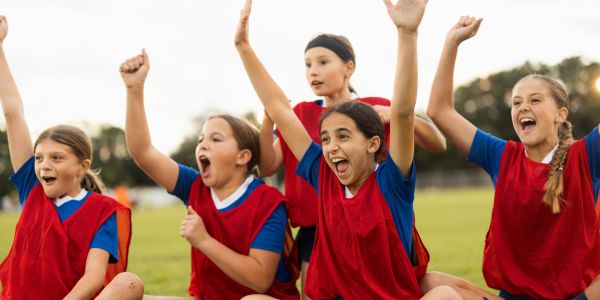 Young girls in red sports vests cheering outdoors.