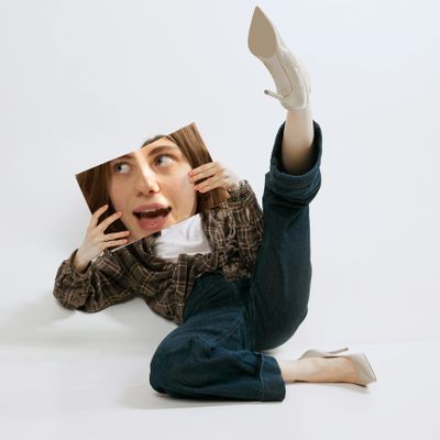 Person holding a mirror reflecting their face while posing with one leg raised.