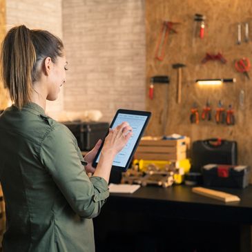 Woman using a tablet in a workshop with tools on the wall.