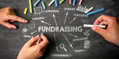 Hands drawing a fundraising strategy diagram on a chalkboard with colorful chalk.