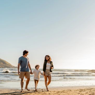 Family of three walking on the beach at sunset.